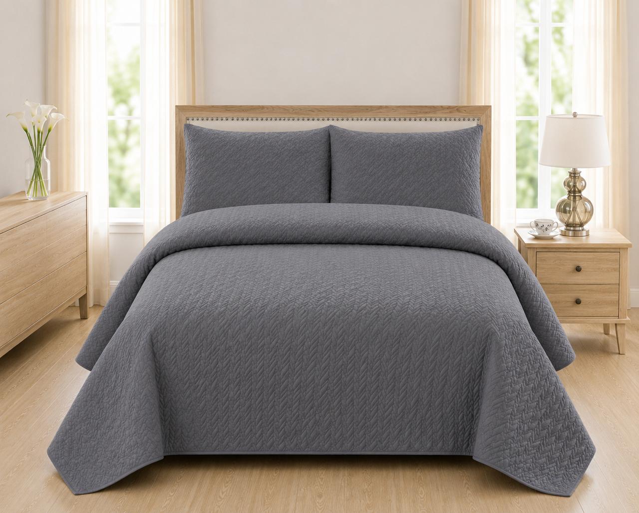 Grey quilted 3-piece bed spread set with two matching pillow shams on a made bed