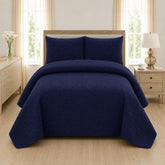 Navy blue quilted 3-piece bed spread set with two matching pillow shams on a made bed