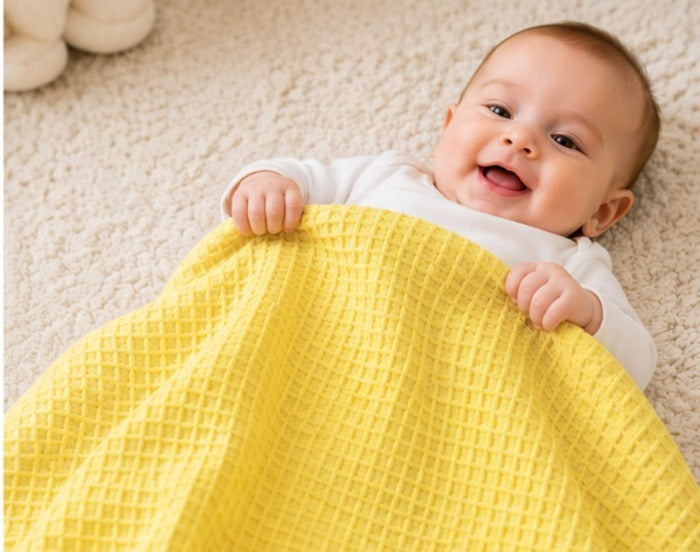 Smiling baby under a yellow honeycomb waffle cotton blanket