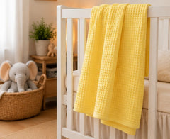 Yellow honeycomb waffle baby blanket draped on a white crib