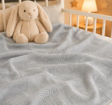 Grey cellular cotton baby blanket on a cot with a bunny