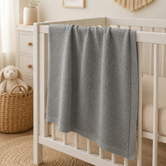 Grey waffle baby thermal blanket on a crib