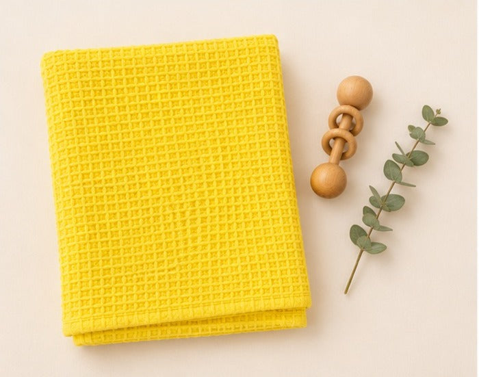 Yellow honeycomb waffle cotton baby blanket folded with wooden rattle