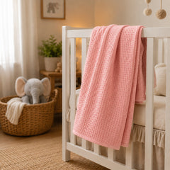 Pink waffle baby thermal blanket draped on a crib