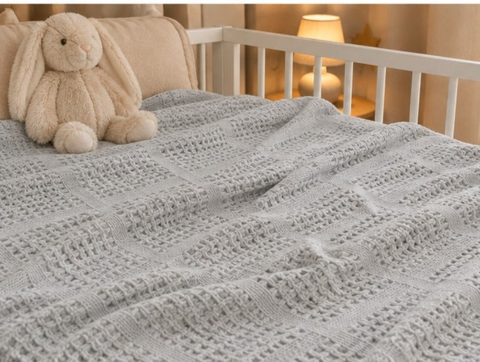 Grey basketweave baby blanket on a cot