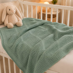 Sage green basketweave baby blanket on a cot
