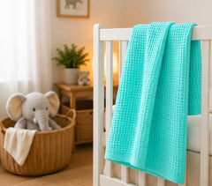 Turquoise honeycomb waffle baby blanket draped on a white crib