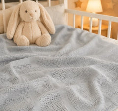 Grey cellular baby blanket on a cot with a bunny